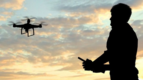 Com um céu nublado, de tons azuis-escuros e roxos como fundo, as imagens a contra-luz de um drone a funcionar, em cima à esquerda, e de um homem a manipulá-lo, em baixo, à direita.